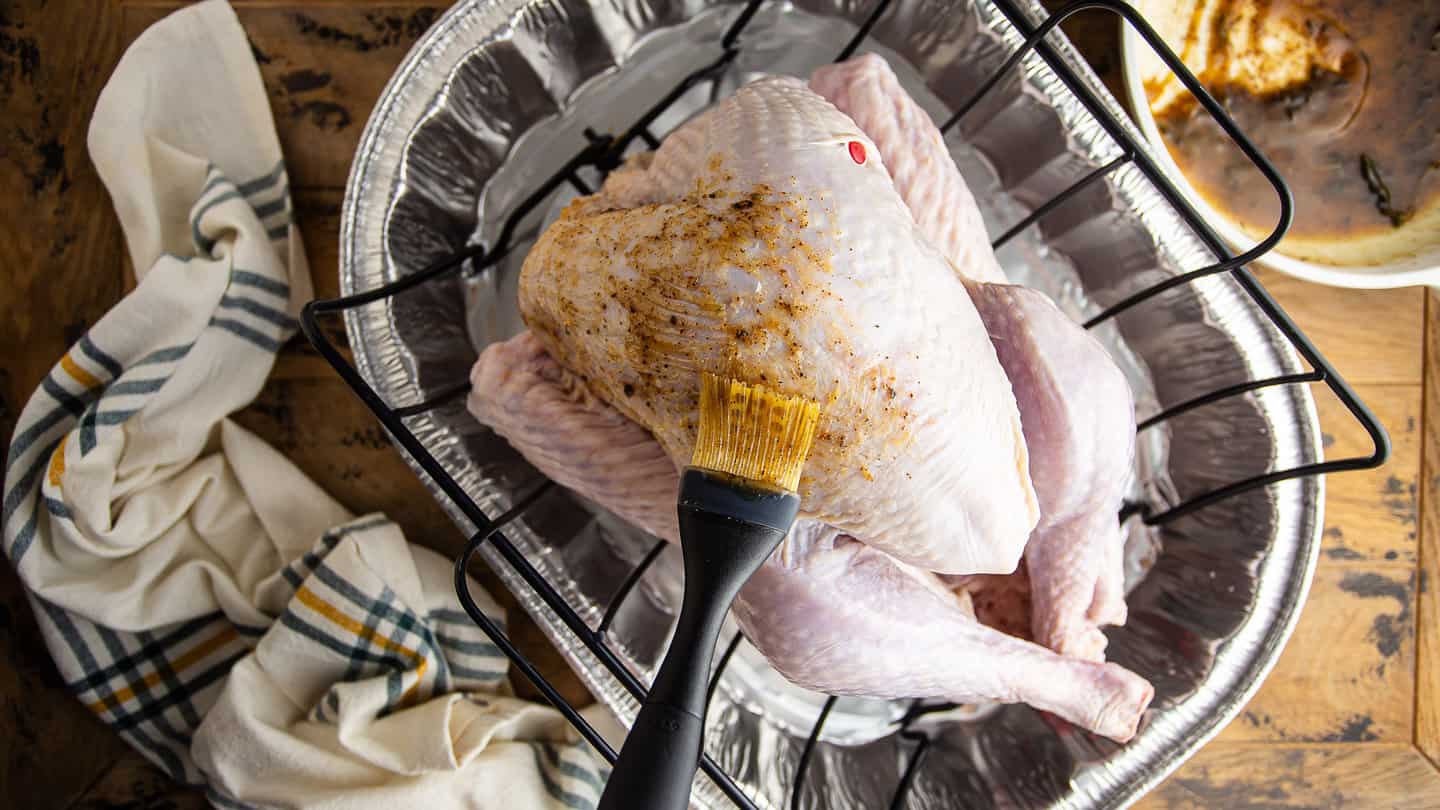 Brushing an uncooked turkey with maple and sage brown butter glaze.