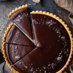 Caramel chocolate tart with a slice cut out and a spoonful of flaked sea salt nearby.