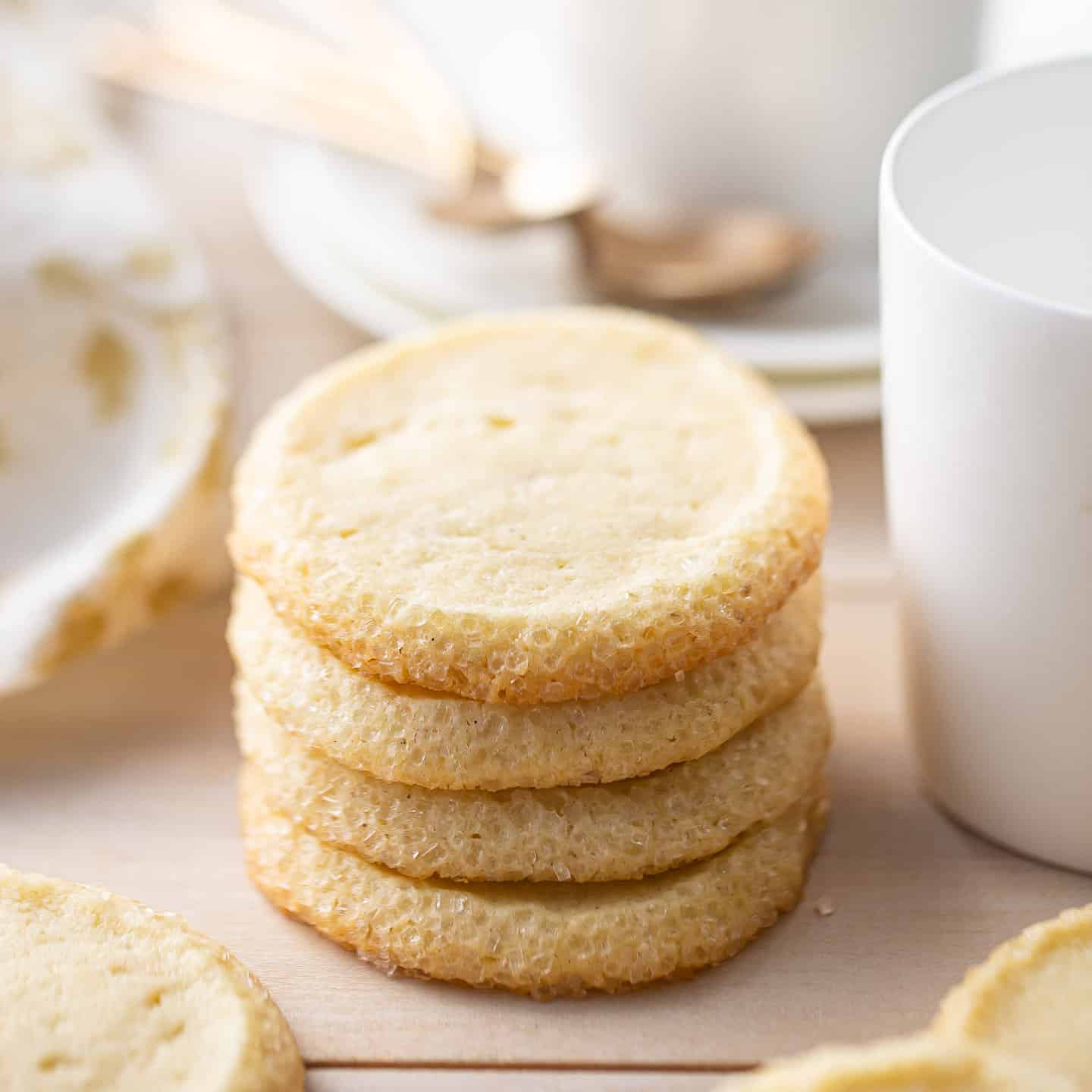 Butter cookies stacked with tea cups and spoons.