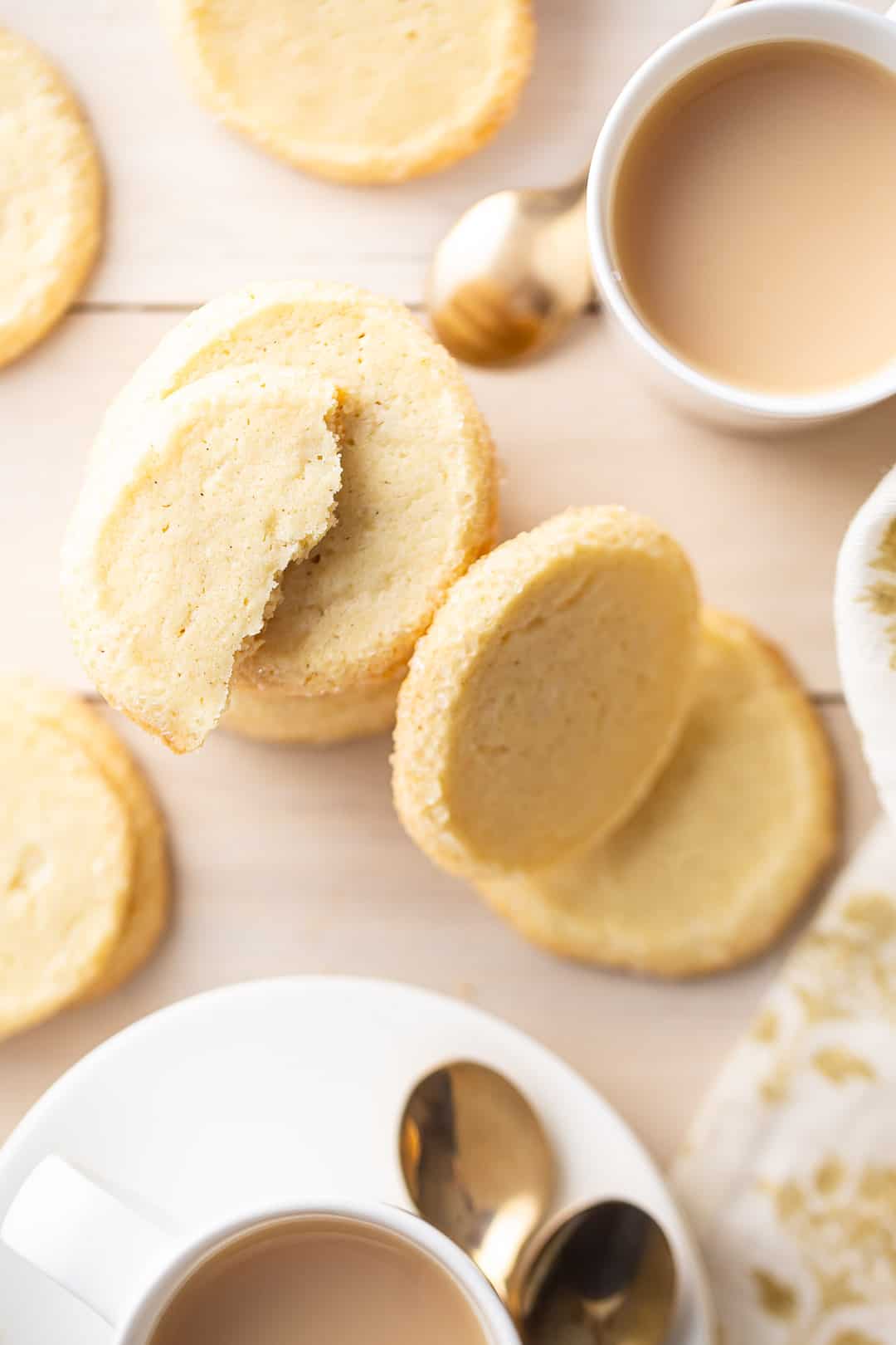 Butter cookies recipe, prepared and scattered over a blond wood tabletop, with cups of milky tea.