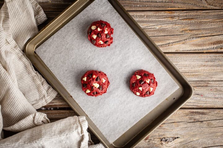 Unbaked red velvet chocolate chip cookies on a parchment-lined baking sheet.