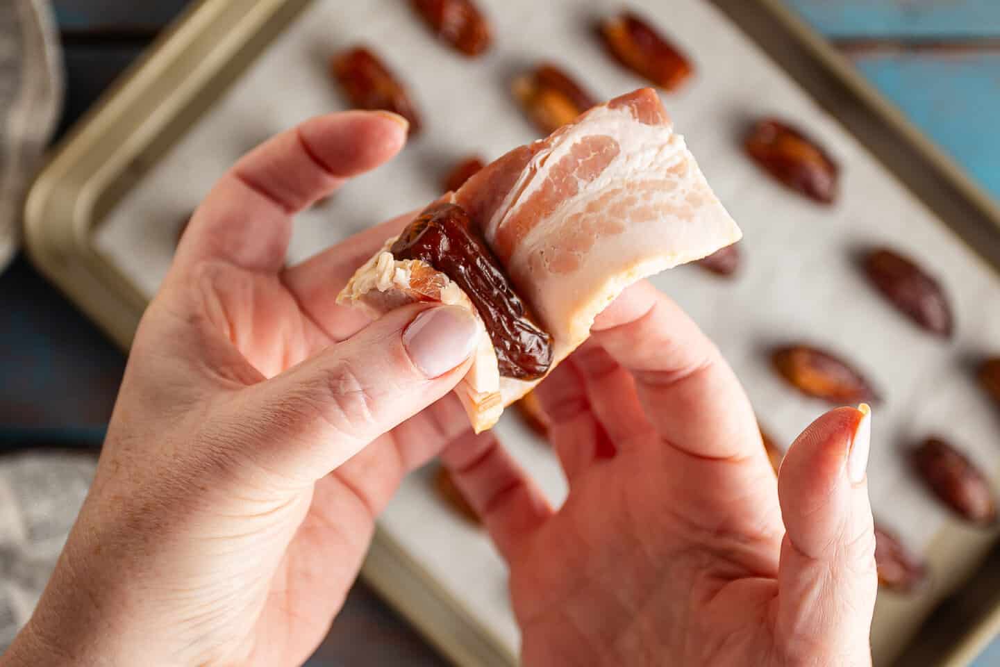 Wrapping a thick slice of bacon around a stuffed date.