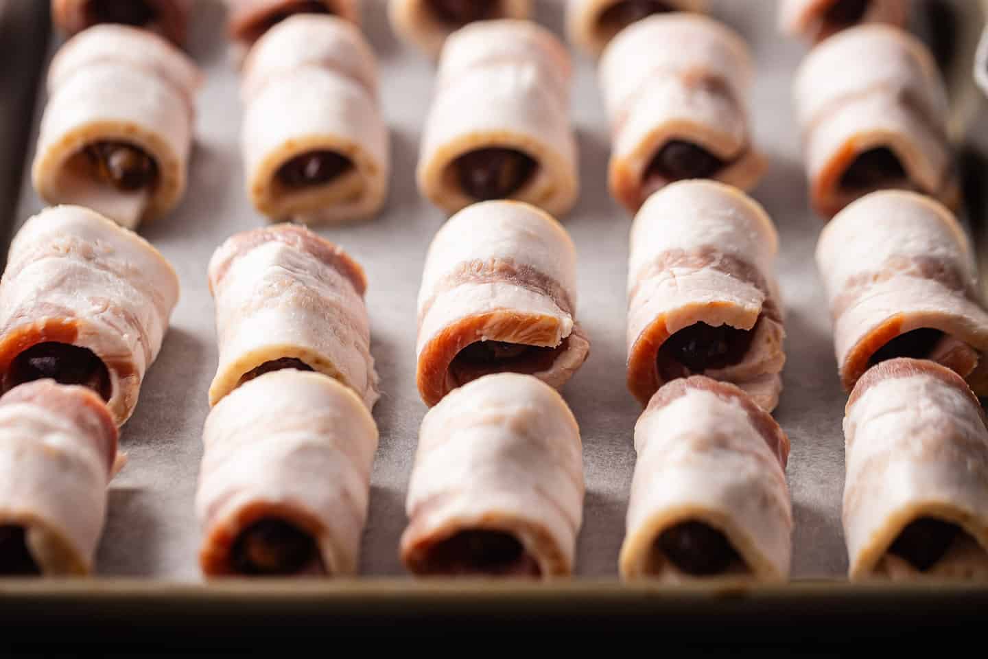 Bacon wrapped dates on a parchment-lined baking sheet.