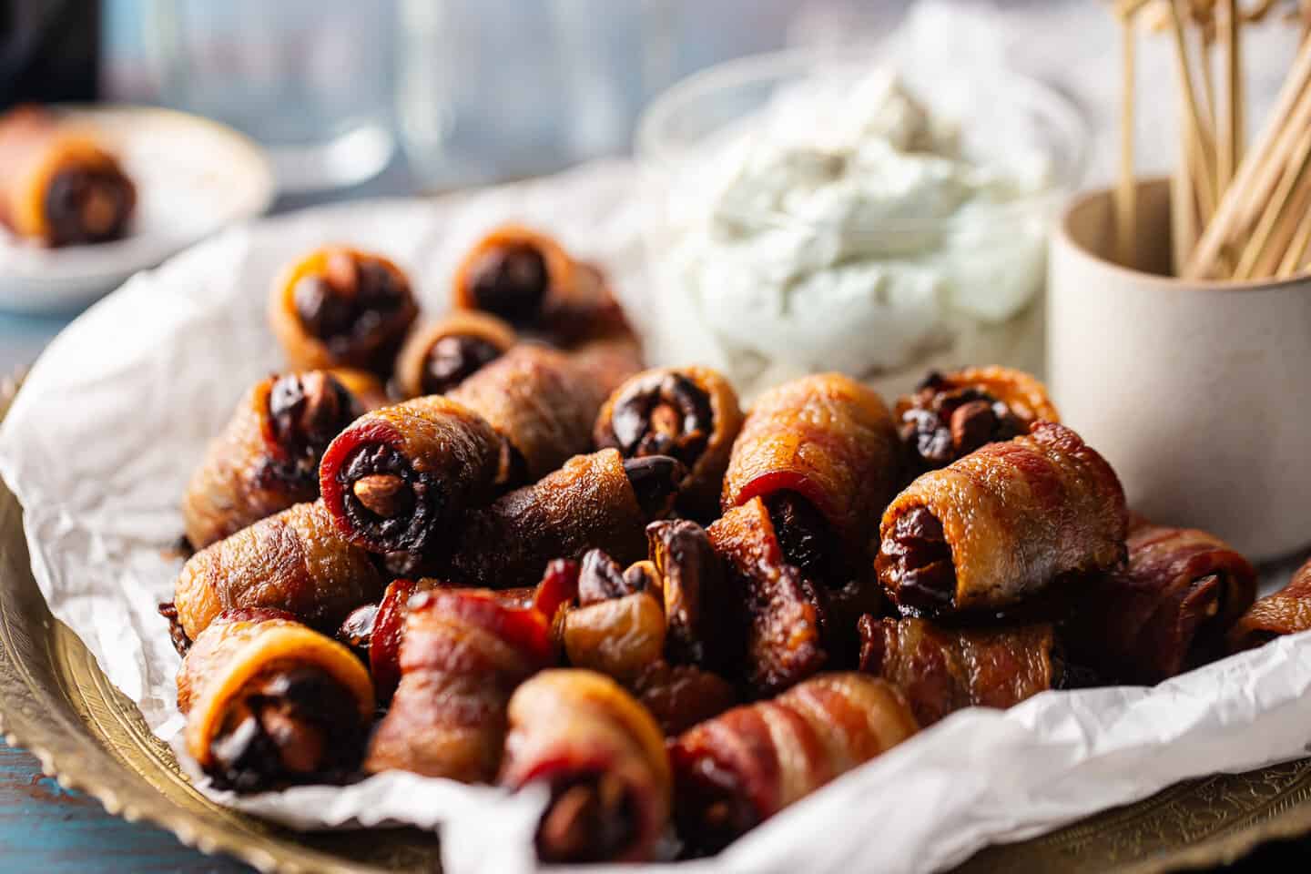 A tray piled high with bacon wrapped stuff dates, served alongside a whipped blue cheese dip.