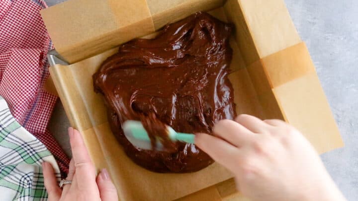Smoothing warm fudge into an even layer in the pan.