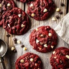 Red velvet cookies with white chocolate chips, arranged on a distressed wooden surface with a vintage ice cream scoop.