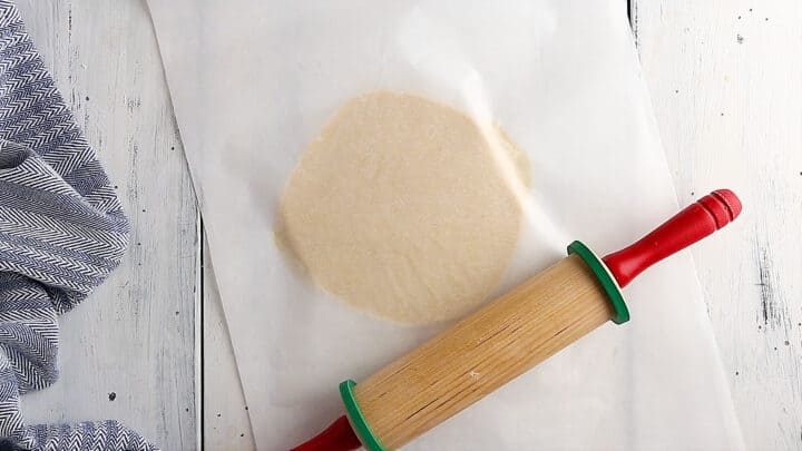 Rolling sugar cookie dough out between two sheets of parchment paper.