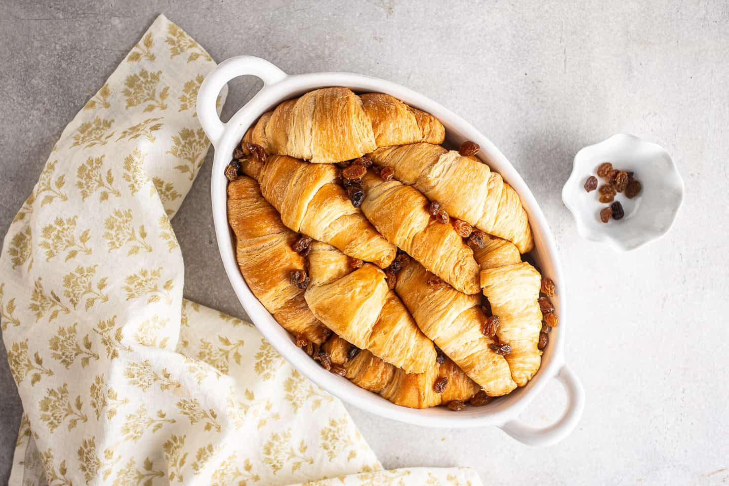 Croissants and golden raisins arranged in a baking dish.