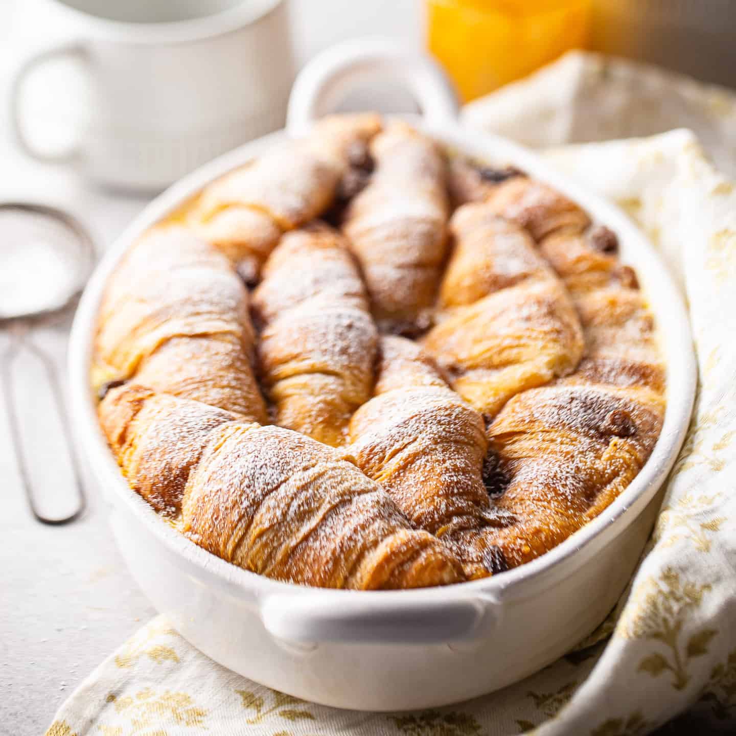 Croissant bread pudding baked in an oval dish with powdered sugar on top.