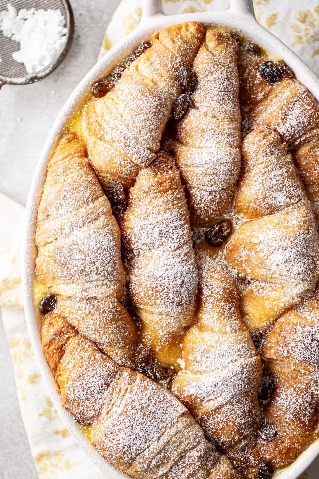 Bread pudding with croissants recipe, speckled with golden raisins and dusted with powdered sugar.