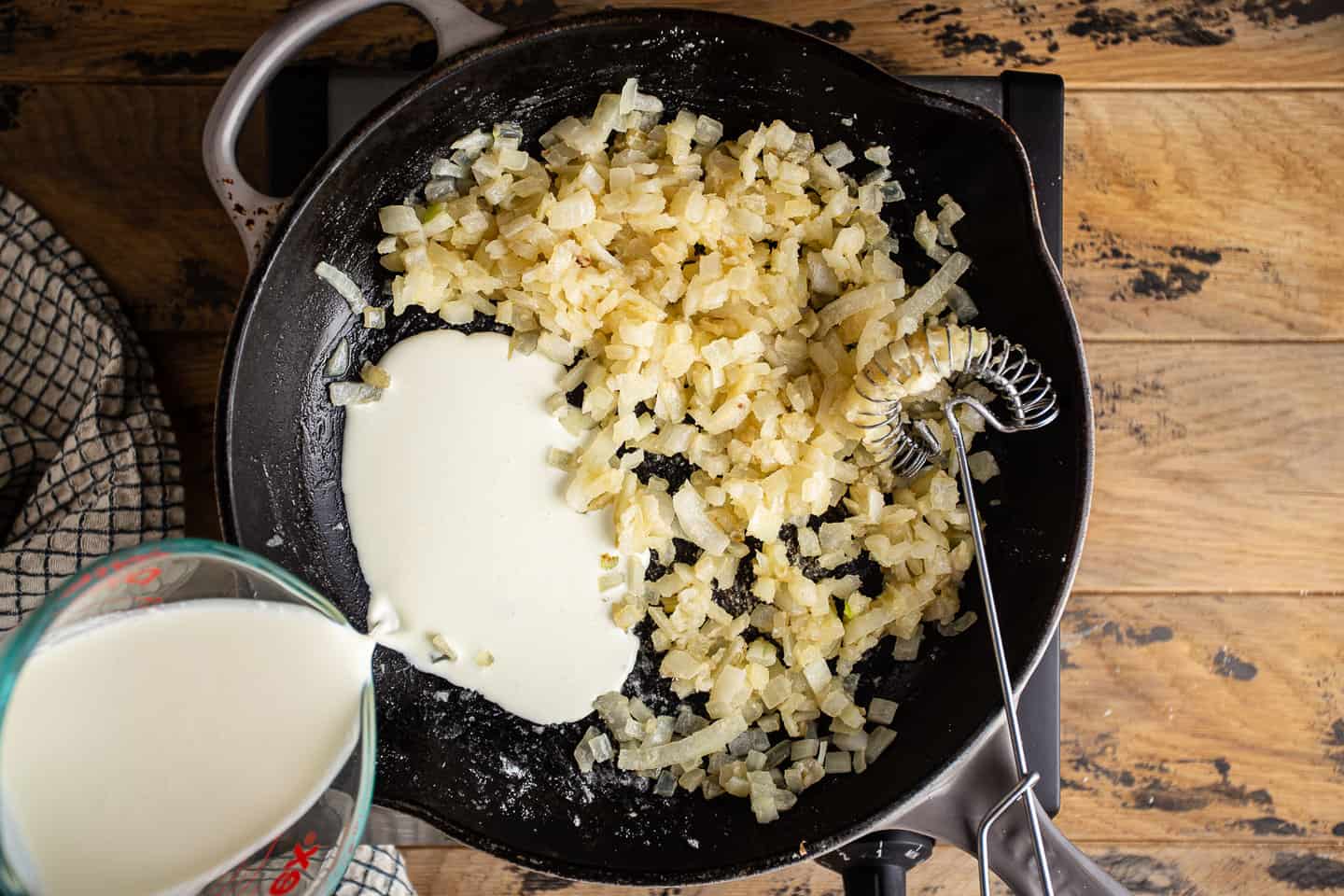 Pouring cream into onions and roux to make a cream sauce.