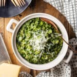 Creamed spinach in a ceramic pot with parmesan cheese.