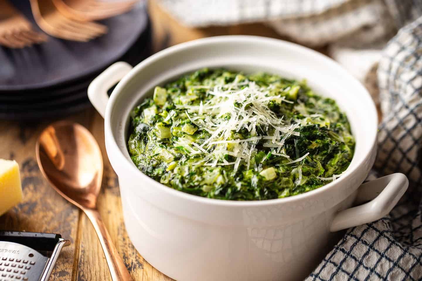 Cream spinach recipe, prepared and presented in a white serving dish with grated parmesan on top.