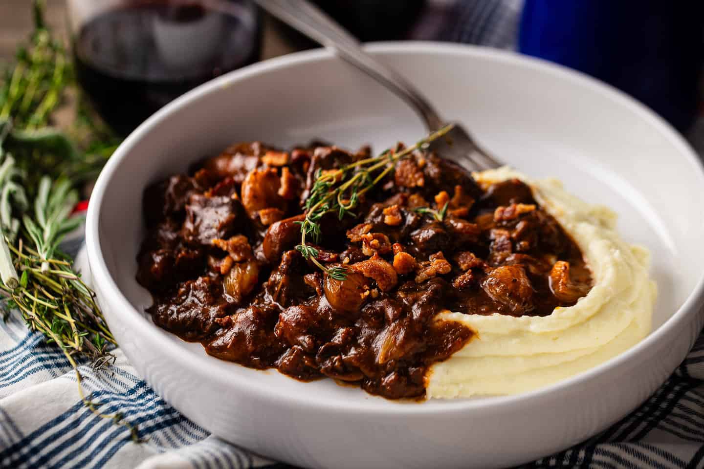 Julia Child inspired beef bourguignon recipe, made with aromatic herbs and spooned into a shallow bowl.
