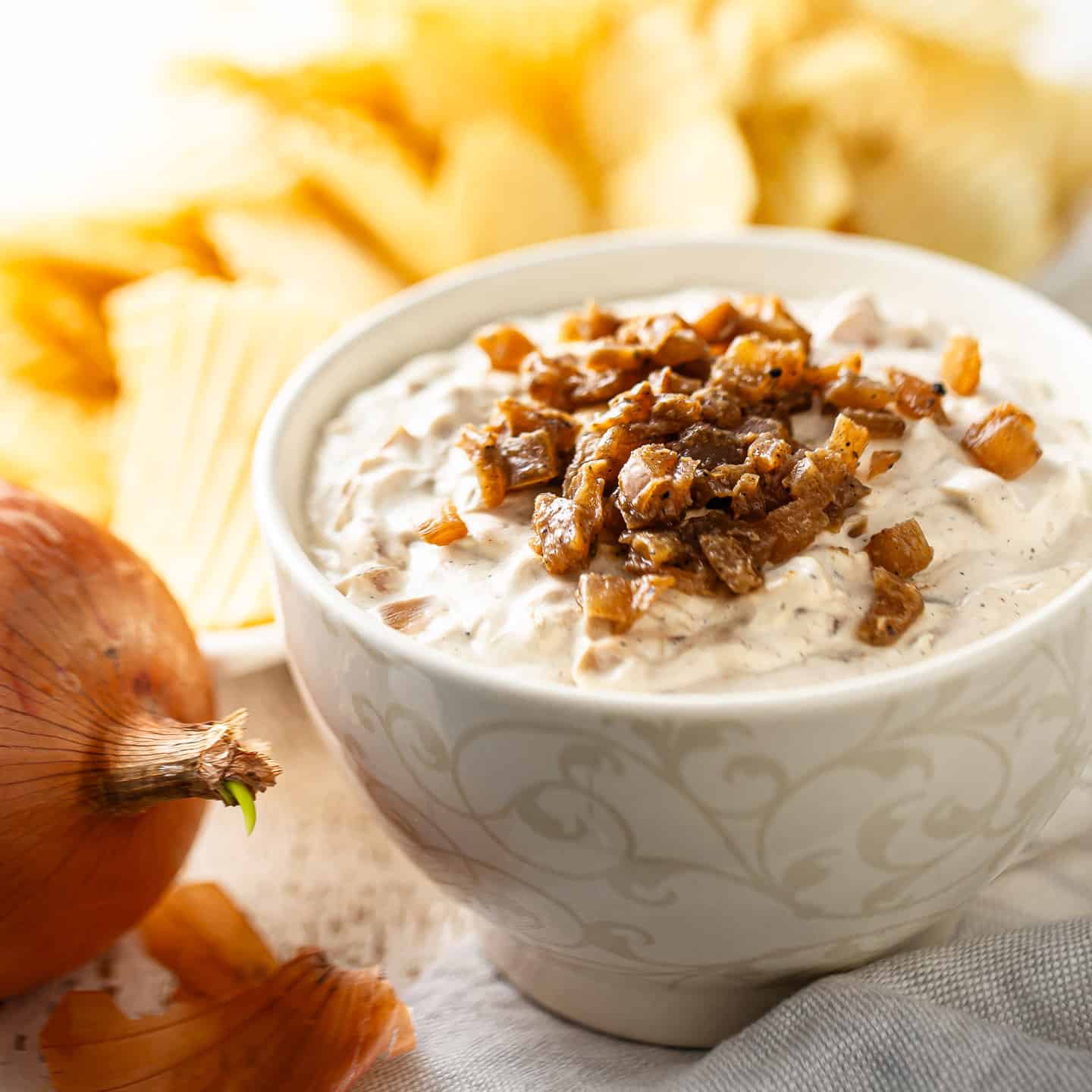 French onion dip presented in a bowl with potato chips in the background.