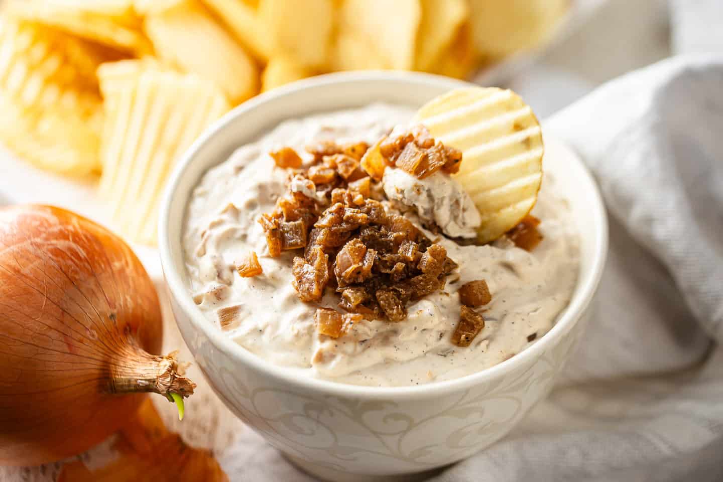 Dipping a potato chip into a bowl of caramelized onion dip.