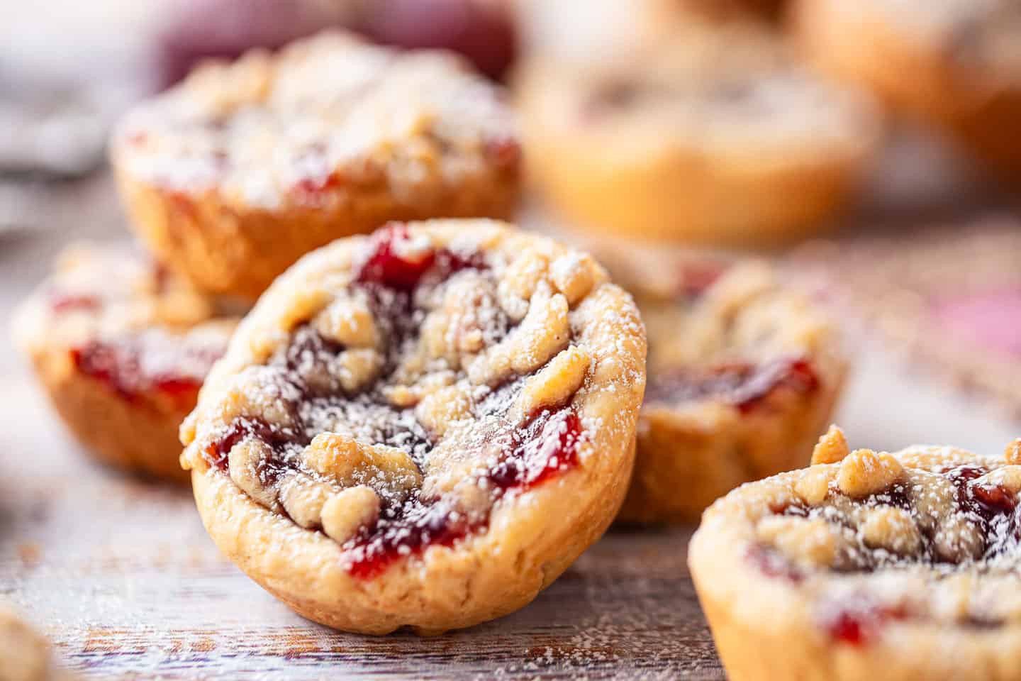 Raspberry tartlets filled with jam and topped with streusel and powdered sugar.