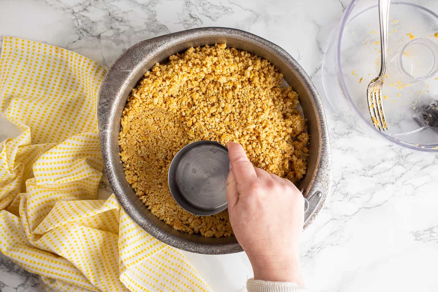 Pressing lemon shortbread crust into the bottom of a cake pan with a measuring cup.