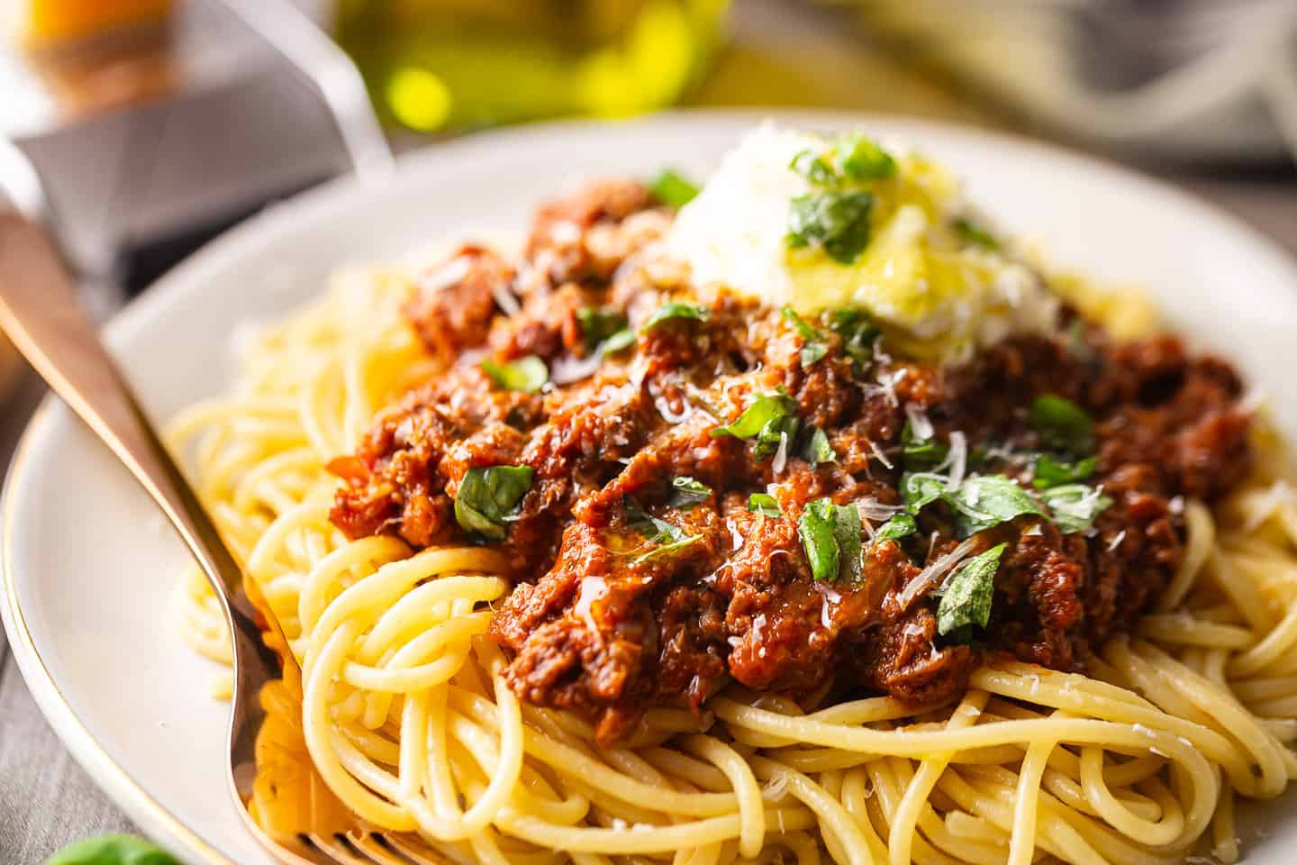 Spaghetti Bolognese garnished with fresh basil, ricotta, parmesan, and olive oil.