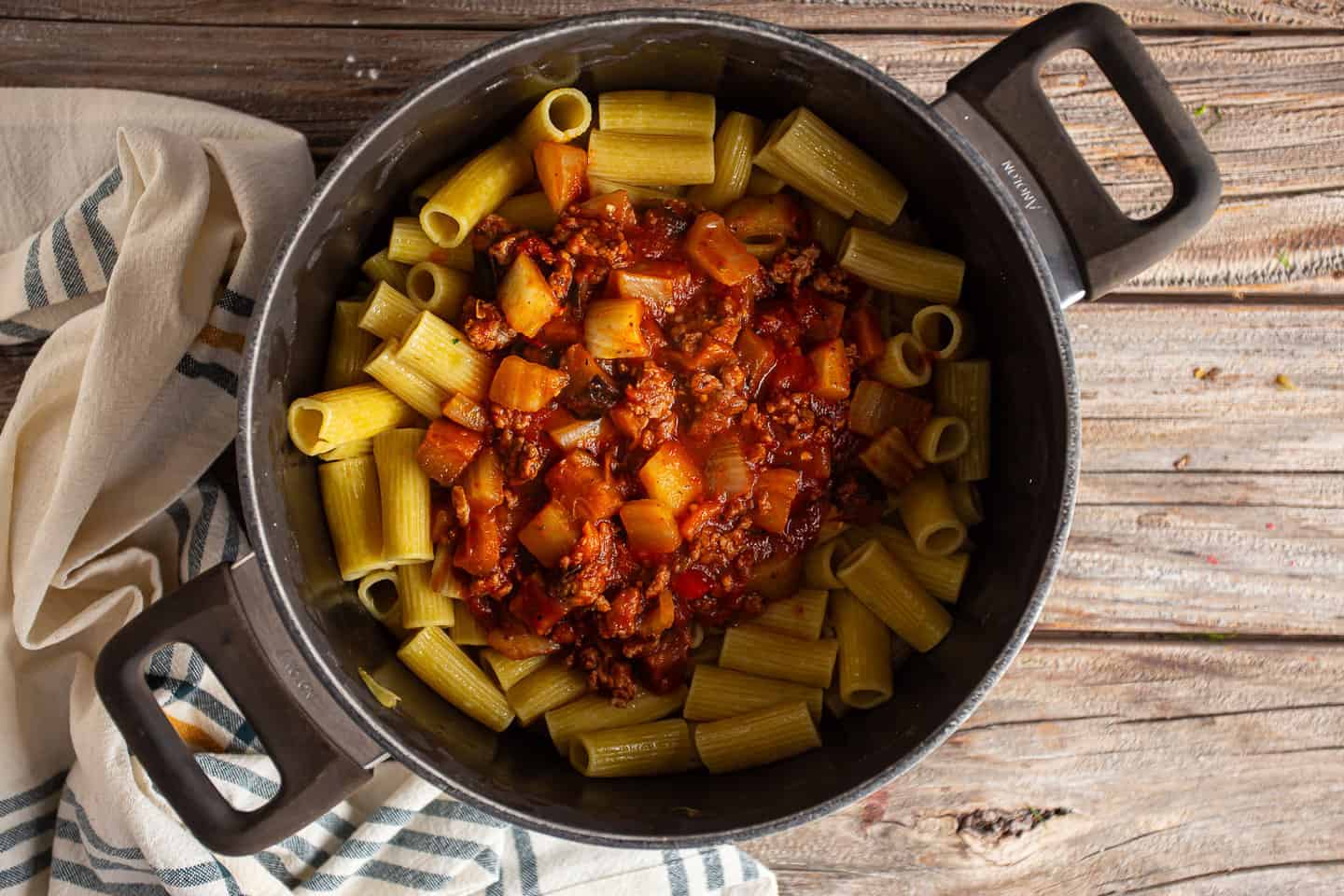 Tossing cooked rigatoni with sauce, sausage, and vegetables.