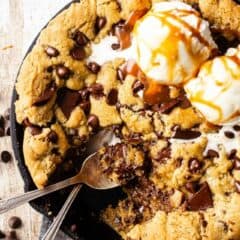 Skillet chocolate chip cookie with two vintage silver spoons.