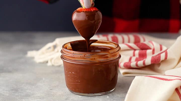 Dipping a fresh strawberry in smooth melted chocolate and allowing the excess to drip away.