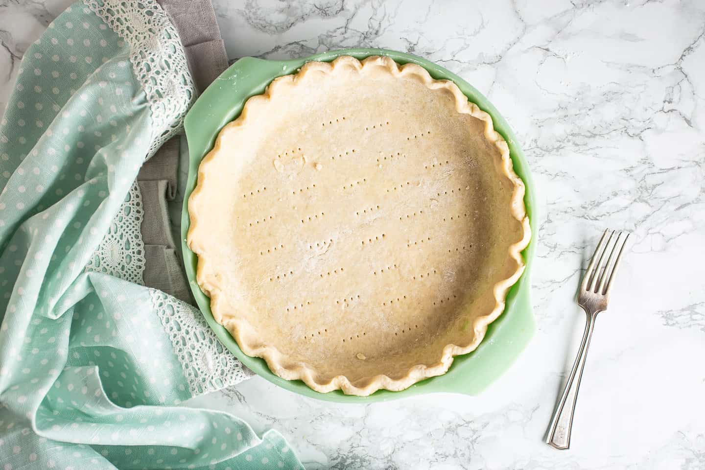 A docked, unbaked pie crust in a green pie dish.