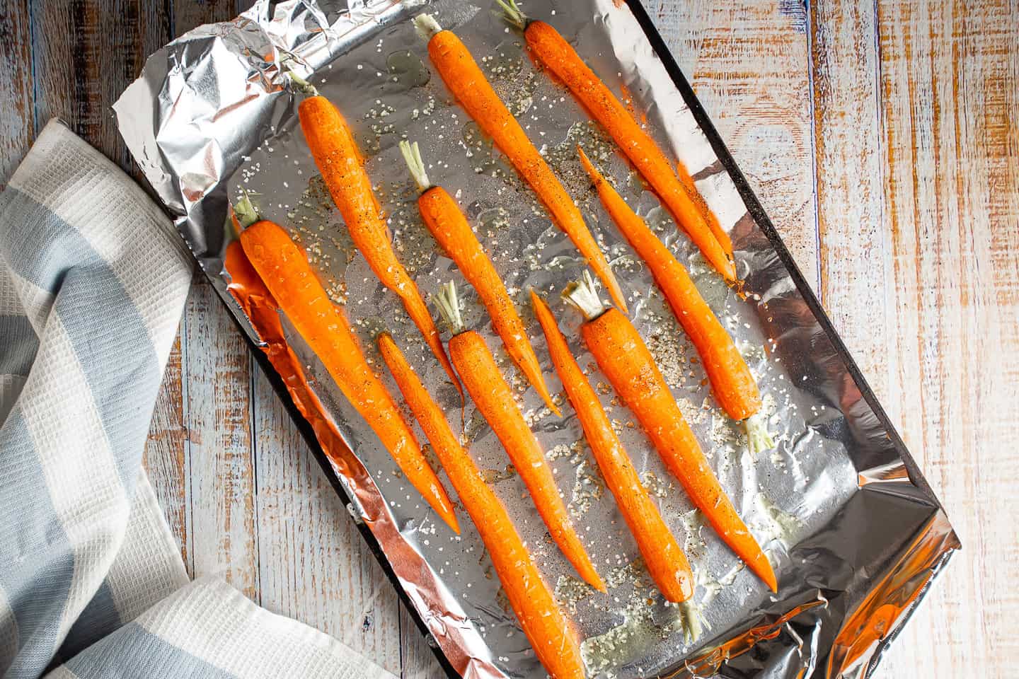 Raw carrots drizzled with olive oil and seasoned with salt and pepper, on a foil-lined sheet tray.