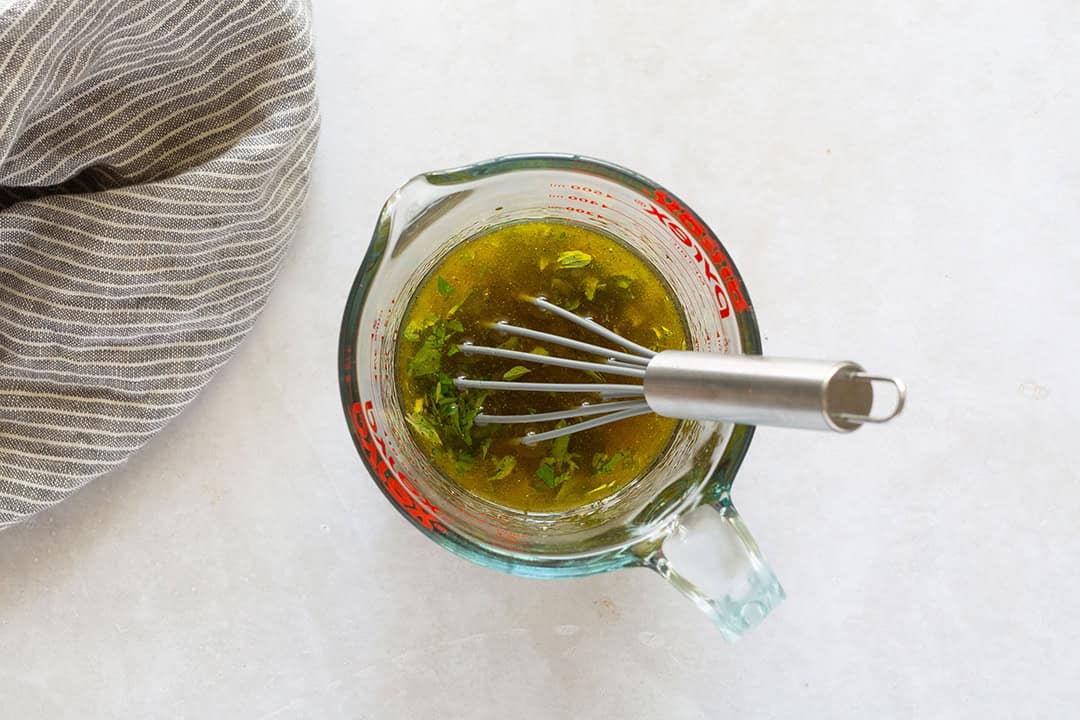 Greek salad dressing in a liquid measuring cup with a whisk.