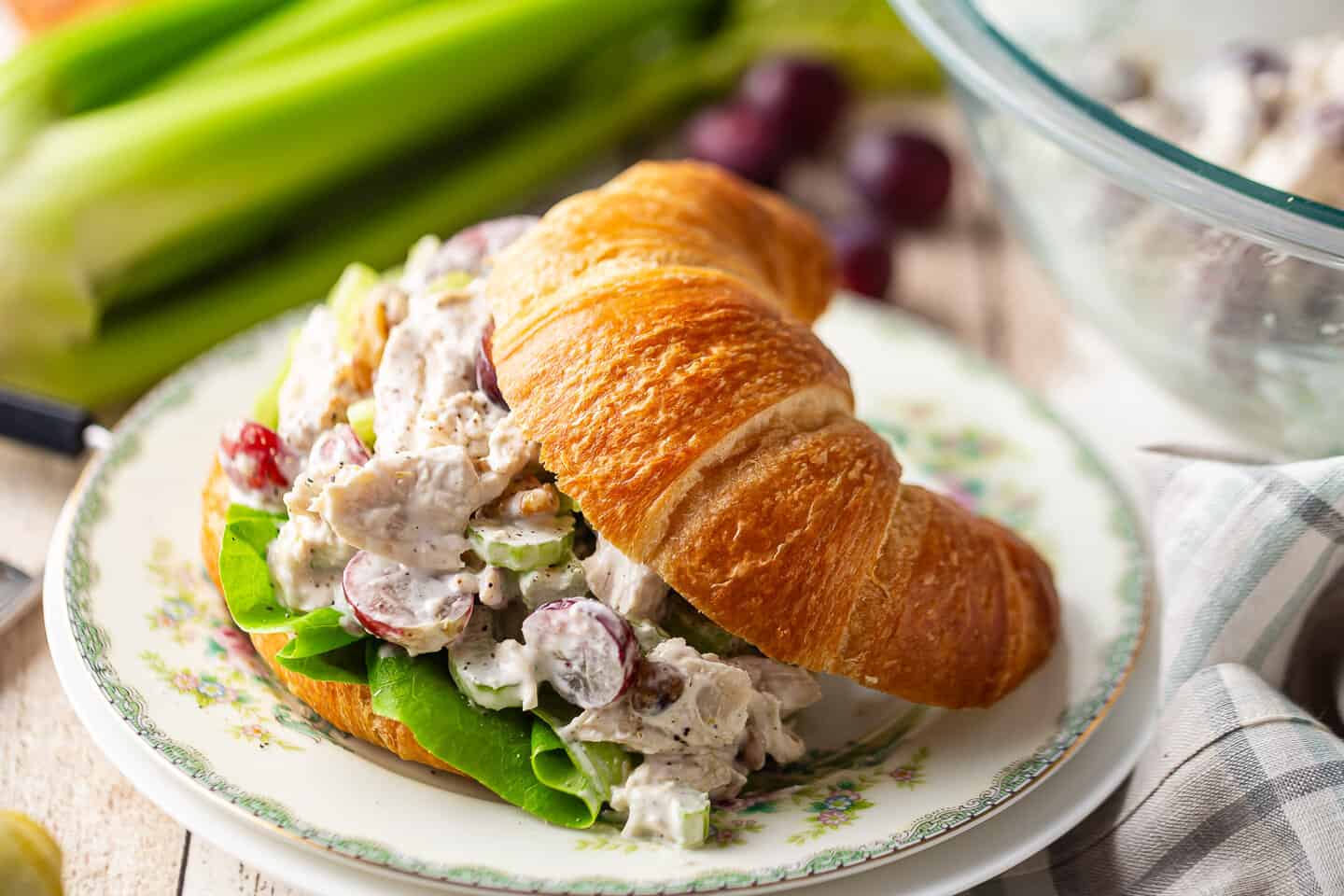 A recipe for chicken salad, served on a croissant with celery and grapes in the background.
