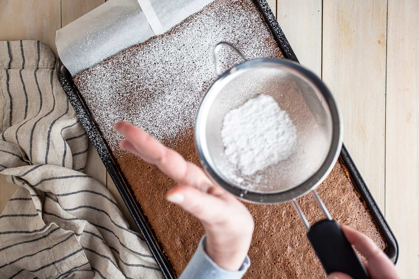 Dusting Swiss roll cake with powdered sugar to prevent sticking.