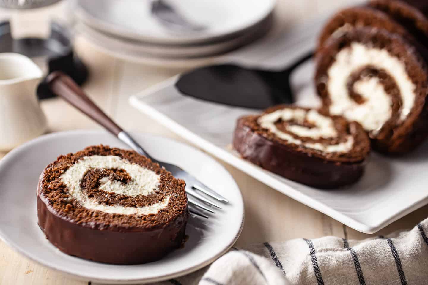 Recipe for Swiss cake roll, prepared, sliced, and served on a white wood tabletop.