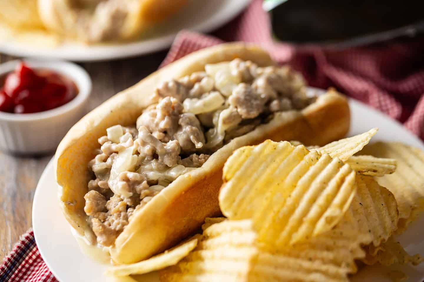 Chicken cheesesteaks recipe, prepared and served with potato chips and ketchup on the side.