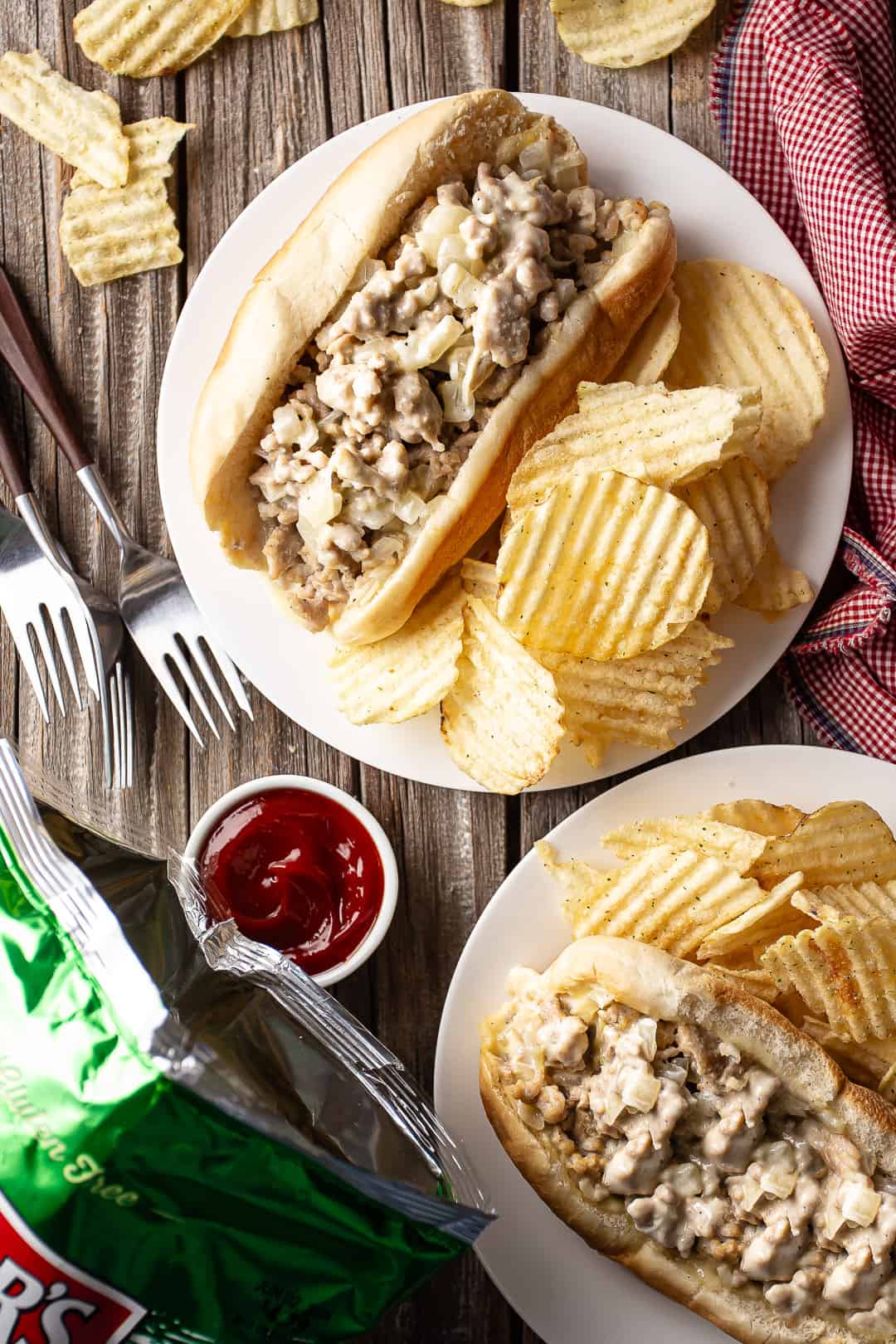Chicken cheese steaks served with chips on a distressed wooden tabletop.