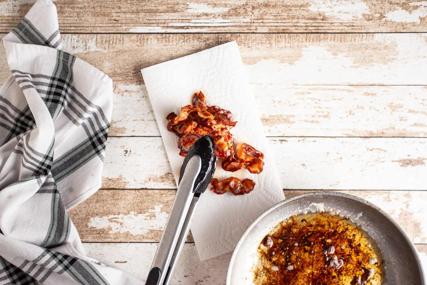 Removing cooked bacon from the pan and placing it on paper towels to drain.