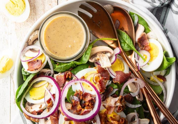 Spinach salad with warm bacon dressing in a shallow white bowl.