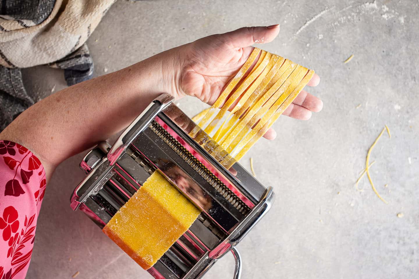 Cutting homemade pasta sheets into wide noodles with a pasta maker.