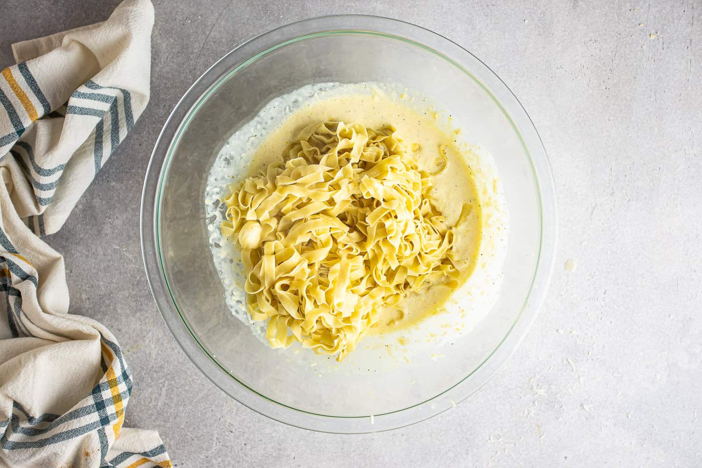 Adding cooked and buttered pasta to the creamy lemon sauce.