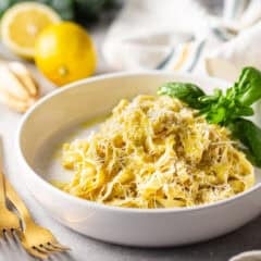 A tangle of lemon pasta in a shallow bowl with a sprig of fresh basil.