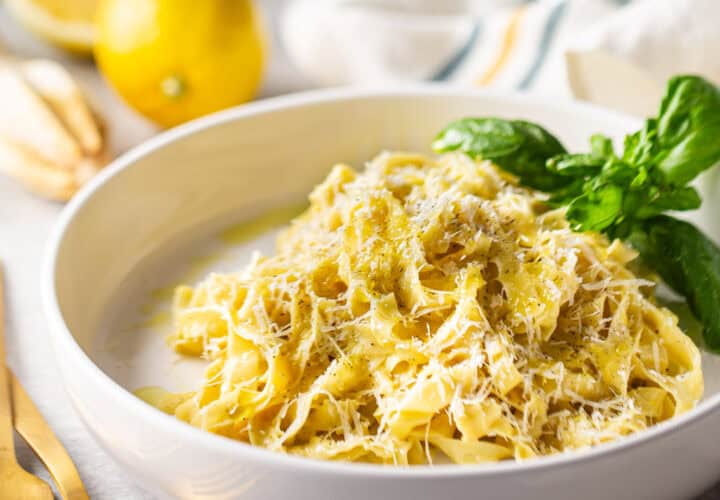 A tangle of lemon pasta in a shallow bowl with a sprig of fresh basil.