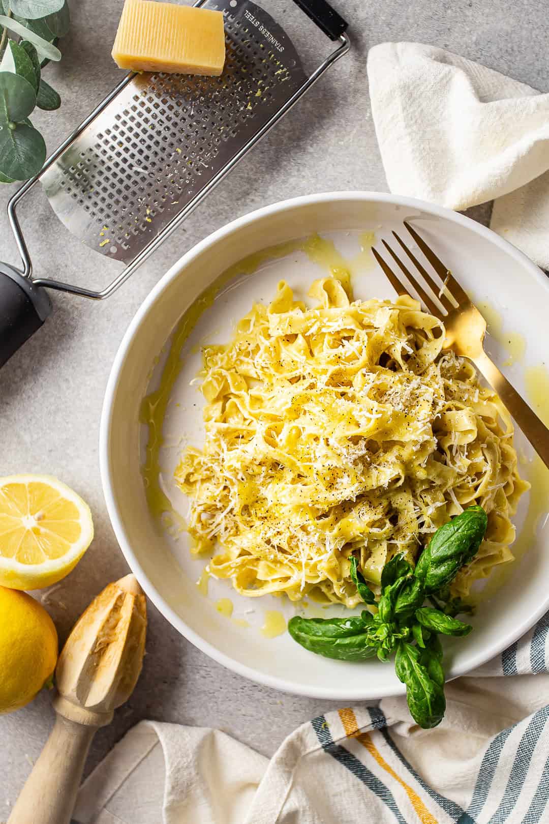 Creamy lemon pasta presented on a gray tabletop with lemons and parmesan cheese.
