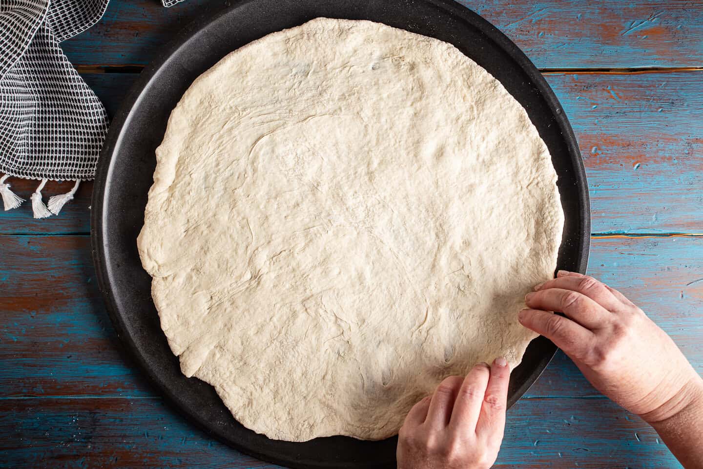 Stretching pizza dough over a pizza pan.