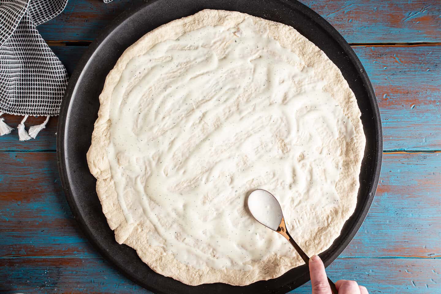 Spreading ranch dressing over pizza dough with the back of a spoon.