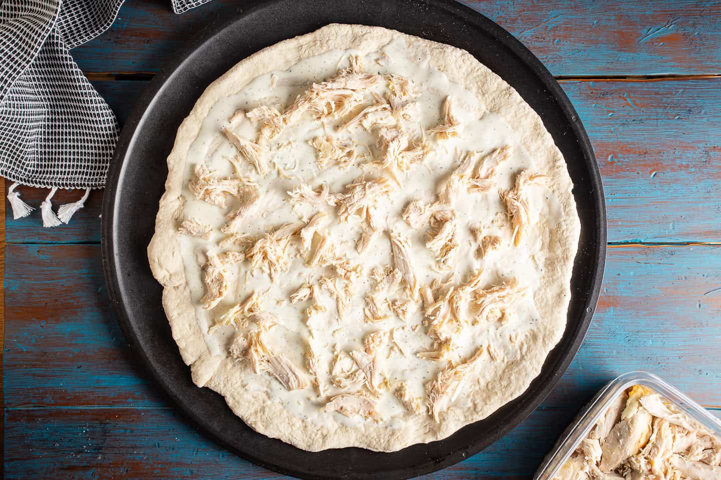 Topping pizza with cooked shredded chicken.