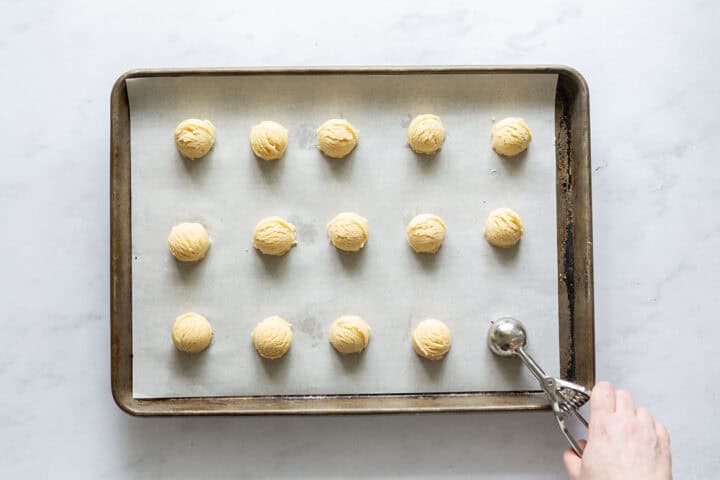 Lemon cookie batter being scooped onto a sheet pan