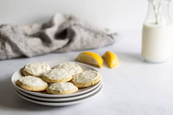 Frosted lemon cookies on a plate next to a bottle of milk.