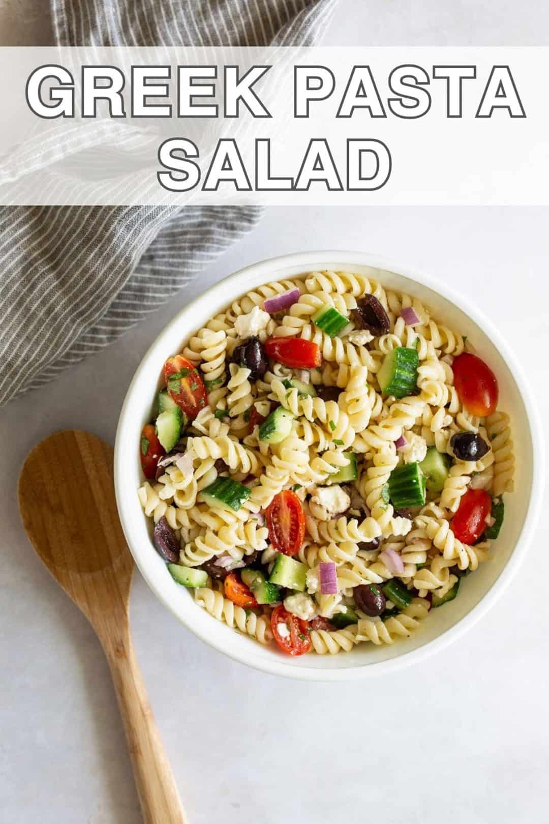 A bowl of Greek pasta salad recipe with a spoon and text overlay.