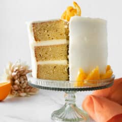 three layer orange creamsicle cake with slice cut on cake stand with orange napkin.