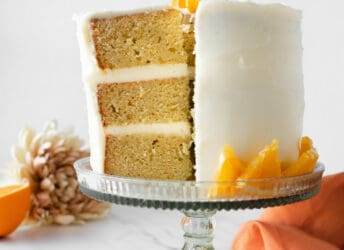 three layer orange creamsicle cake with slice cut on cake stand with orange napkin.