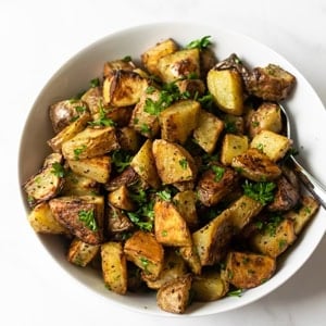 oven roasted potatoes in a white bowl with a serving spoon.